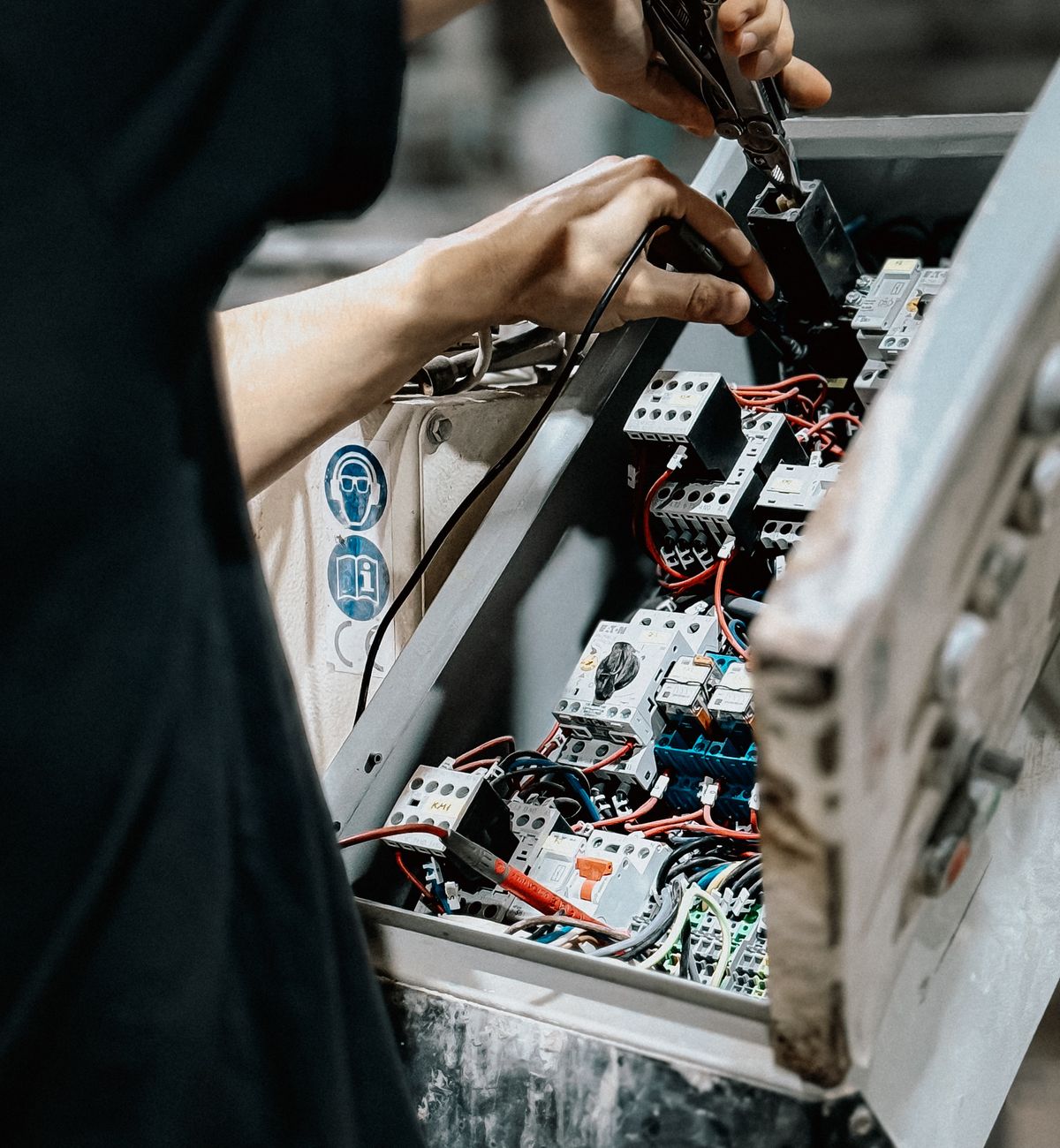 Un électricien intervient dans une armoire de commande ouverte.