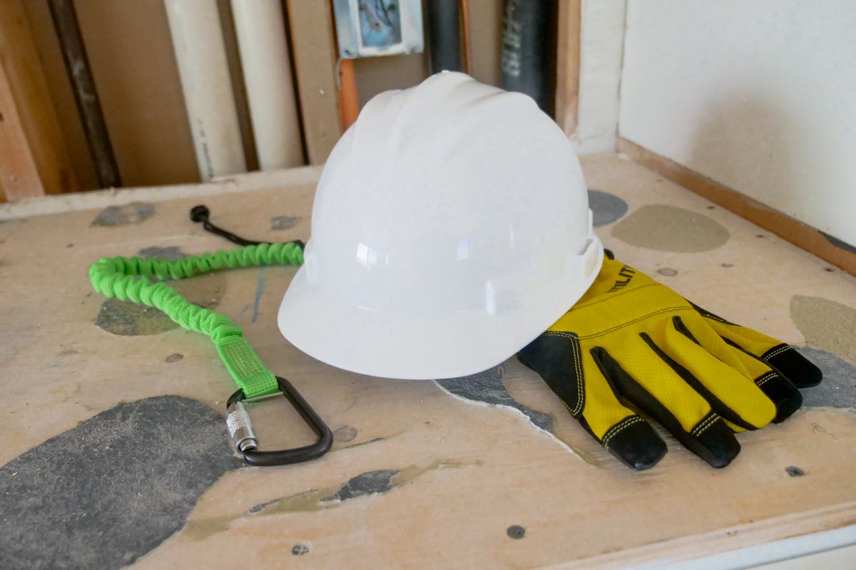 Un casque de chantier, des gants et une longe posés sur un établi.